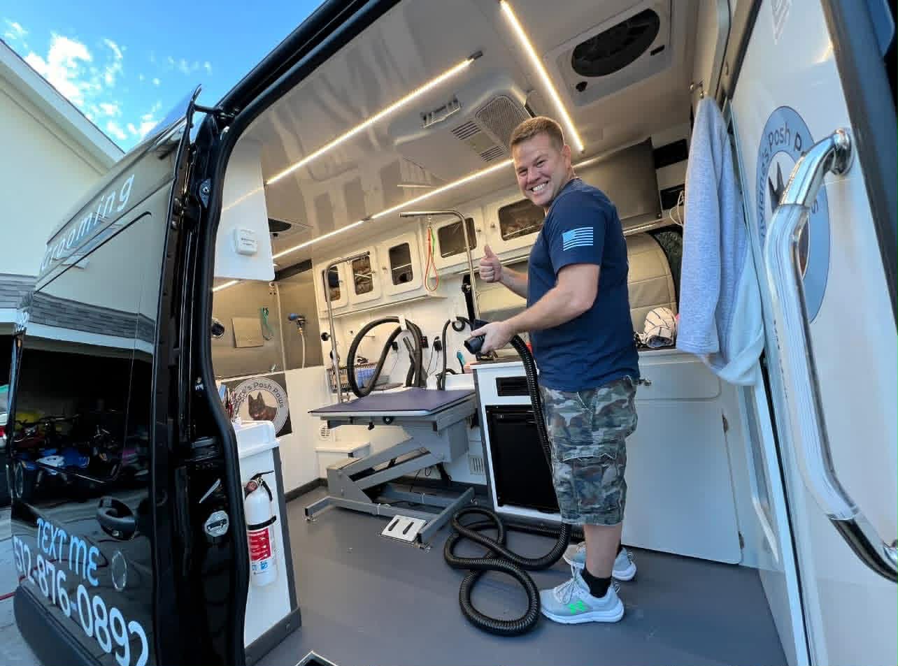 The open side door of the Viviane's Posh Paws mobile grooming van, showing the grooming table, tub and dryer hose inside